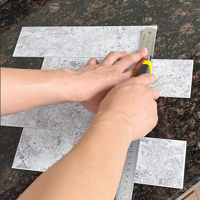 Scoring a peel and stick backsplash tile with a utility knife and metal ruler