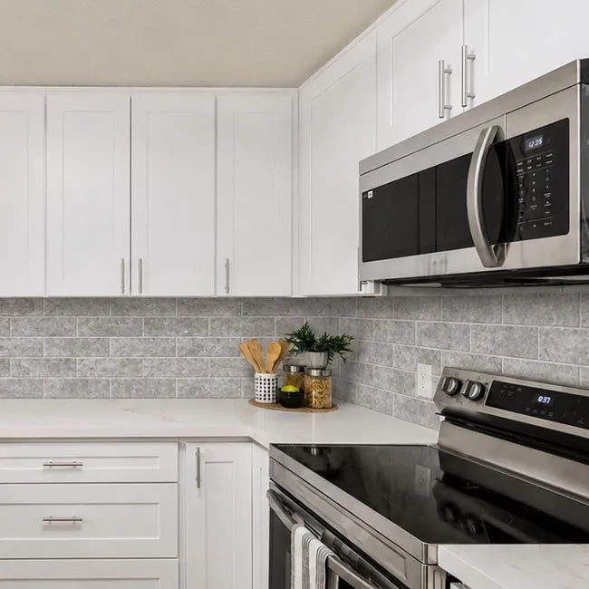 Gray stone peel and stick subway tile backsplash in modern kitchen with white cabinets