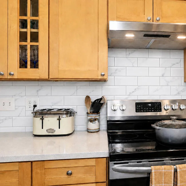 White marble peel and stick subway tile backsplash behind kitchen stove and countertop